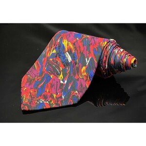 May include: A rolled-up necktie with a vibrant abstract design. The tie features a pattern of brushstrokes in red, blue, yellow, purple, and white against a black background. The tie is made of a smooth, possibly silk, material.