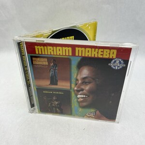 Peut inclure: Un boîtier de CD avec la pochette de l'album de Miriam Makeba. La couverture présente une bannière rouge avec "MIRIAM MAKEBA" en grandes lettres blanches. L'illustration comprend des images de Makeba et le texte "ORIGINAL 2 LPs ON 1 CD".