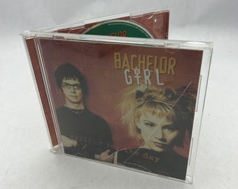 Puede incluir: Estuche de CD con fondo rojo y blanco. La portada presenta una banda llamada "Bachelor Girl" y el texto "Waiting for the day".