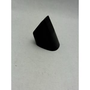 Op de afbeelding: Een zwart, wigvormig object met een afgeronde basis en een geribbelde bovenkant. Het object is gemaakt van een mat materiaal en staat tegen een lichtgrijze achtergrond. Het ontwerp is eenvoudig en geometrisch.