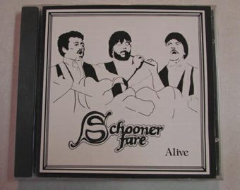 Può includere: Un'immagine di un CD con un'illustrazione in bianco e nero di tre uomini. Il nome della band "Schooner Fare" è visualizzato in caratteri stilizzati, con la parola "Alive" sotto. La custodia è in una custodia di plastica trasparente.