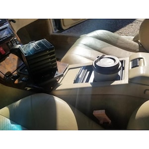 May include: Interior view of a car with tan leather seats and wood trim. A black CD storage case sits on the console, next to a coffee cup with a black lid in the cup holder.