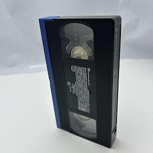 May include: Black VHS tape with a blue spine. The tape has a clear window to view the tape inside. The label reads "Baby Einstein". The tape is angled slightly to the left.