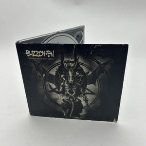 May include: A black CD case with a black and white image of a demonic figure with wings and a snake. The text "BUZZOV*EN" and "VIOLENCE FROM THE VAULT" is printed on the front of the case.