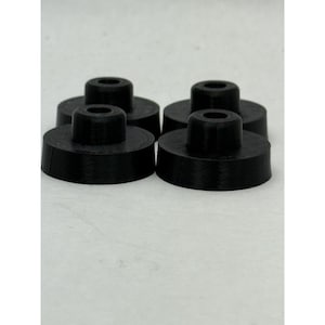 Pode incluir: Quatro objetos pretos, cilíndricos, com um centro circular elevado e um buraco no meio. Os objetos estão dispostos em grupo, com uma vista ligeiramente inclinada, sobre um fundo liso.