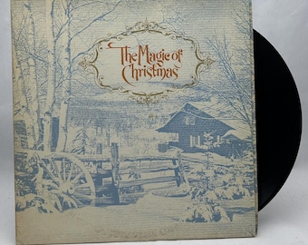 May include: Vintage vinyl record album titled "The Magic of Christmas." The album cover features a winter landscape with a house, trees, and a wooden fence. The title is in an ornate, gold-colored font.