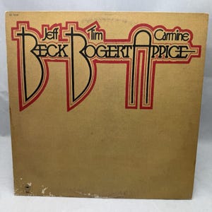 Puede incluir: Una funda de disco de vinilo cuadrada con un fondo texturizado de color tostado. El texto dice Jeff Beck, Tim Bogert y Carmine Appice en una fuente negra estilizada con contornos rojos. El logotipo de Epic es visible en la esquina inferior izquierda con el código KE 32140.