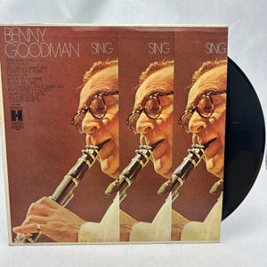 May include: A vintage vinyl record album cover featuring Benny Goodman playing the clarinet. The cover features a close-up of Goodman's face and the text "Benny Goodman Sing Sing Sing" in a bold, white font.