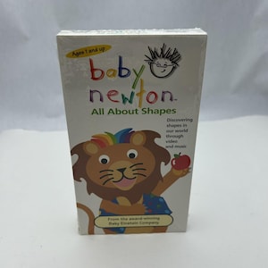 May include: A sealed VHS tape of "Baby Newton: All About Shapes." The cover features a cartoon lion with a rainbow mane holding an apple. Text includes "Ages 1 and up" and "Discovering shapes in our world through video and music."