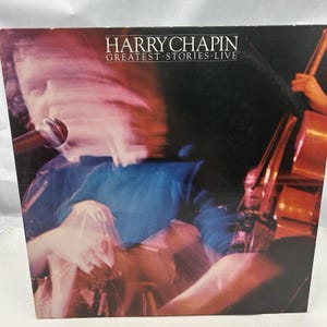 May include: Album cover for "Harry Chapin: Greatest Stories Live." The cover shows a blurred image of a person singing into a microphone, with a double bass in the background. The album title and artist name are in white text.