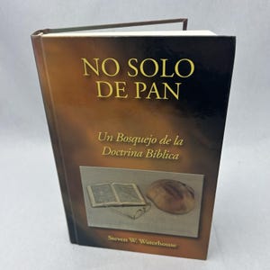Op de afbeelding: Een hardcover boek getiteld "NO SOLO DE PAN" met gouden letters. De omslag bevat een illustratie van een open boek, brood en een bril. De naam van de auteur, Steven W. Waterhouse, staat onderaan.