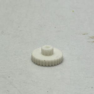 May include: A small, white plastic gear with a central cylindrical hub and toothed outer edge. The gear is designed for mechanical applications and is likely used in a machine or device. The gear is set against a neutral background.
