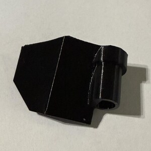 May include: A black, 3D-printed object with a geometric shape. It features a rectangular body with a cylindrical extension. The object is made of solid black material and appears to be a functional component or part.