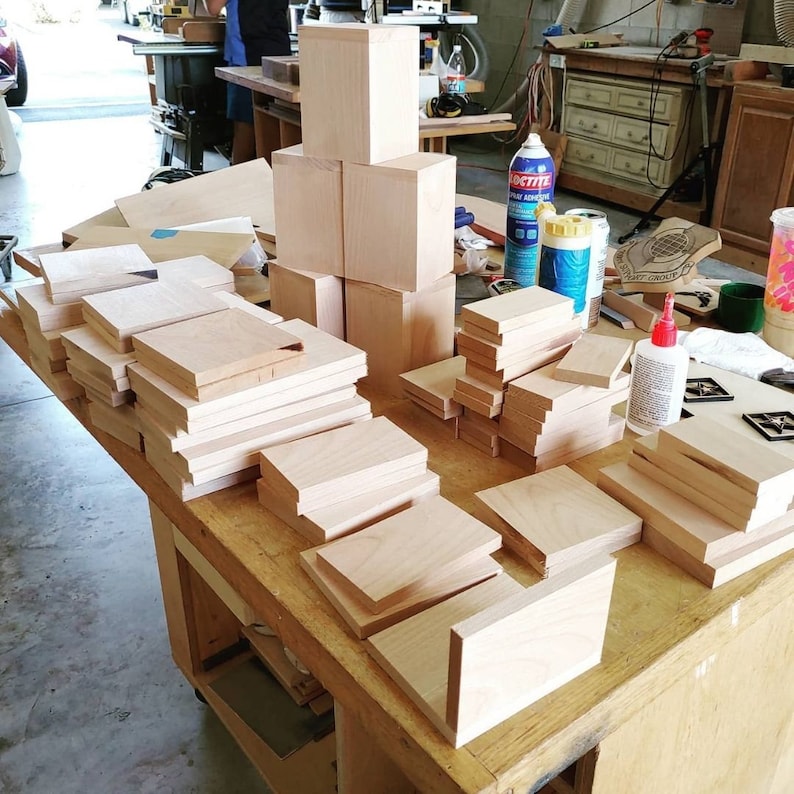 May include: A workbench with a variety of wooden blocks and squares stacked and arranged in different sizes. The blocks are made of light wood and are ready for woodworking projects.