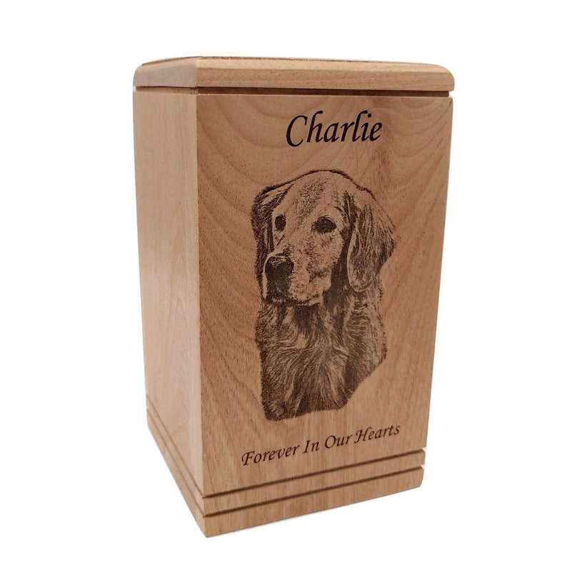 May include: A wooden pet urn with a laser engraved image of a golden retriever. The urn is inscribed with the name "Charlie" and the phrase "Forever In Our Hearts".