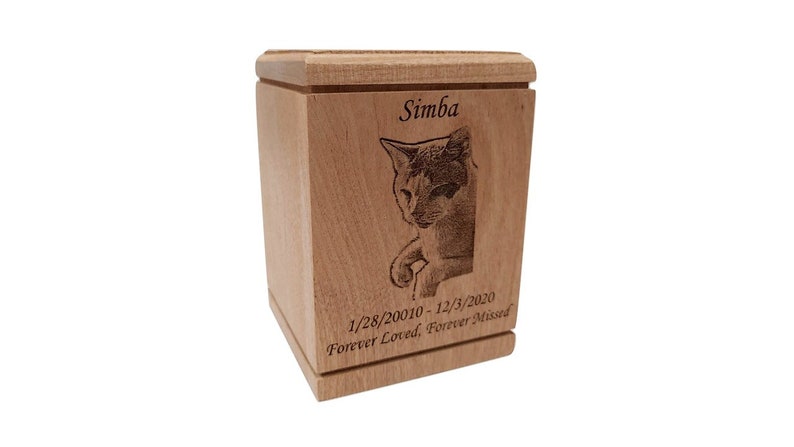 May include: A wooden pet urn with a laser engraved image of a cat and the text "Simba 1/28/20010-12/3/2020 Forever Loved, Forever Missed".