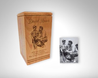 May include: A wooden cremation urn with a laser engraved image of two people playing golf. The urn is inscribed with the name "David Ramos" and a quote about memories.