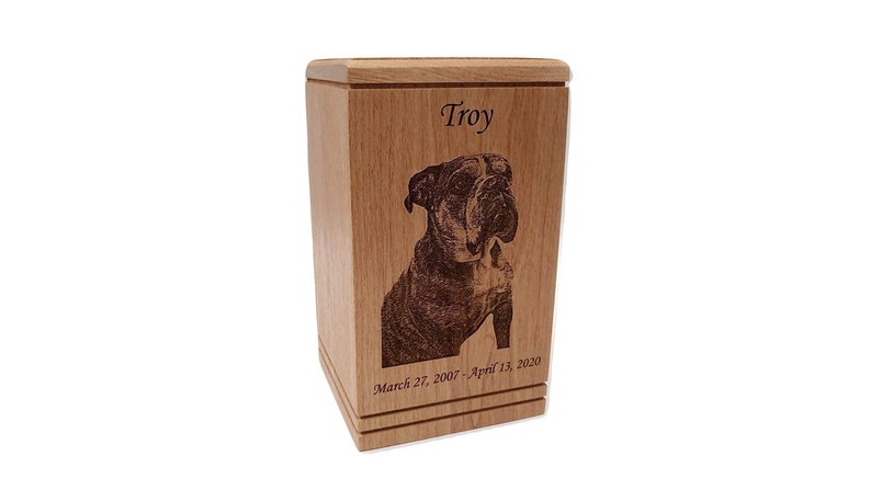 May include: A wooden pet urn with a laser engraved image of a bulldog and the name "Troy" with the dates "March 27, 2007 - April 13, 2020".