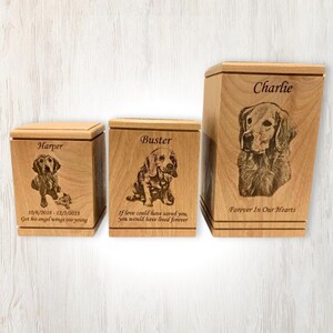 May include: Three wooden pet urns with engraved images of dogs and personalized text. The urns are in different sizes and feature the names "Harper", "Buster", and "Charlie".
