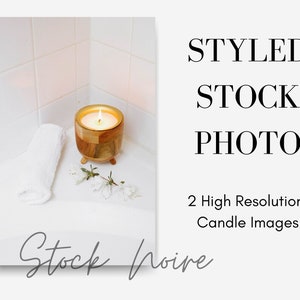 May include: A wooden candle holder with a lit candle inside, a white towel, and white flowers on a white tiled surface.