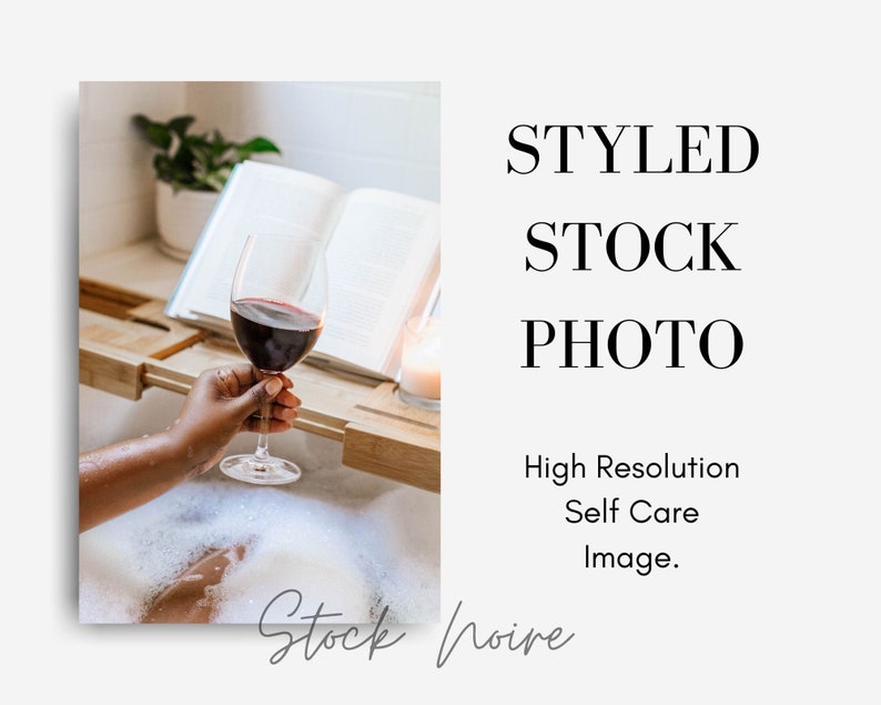May include: A person relaxing in a bathtub filled with bubbles, holding a glass of red wine. A book and a candle are on a wooden tray beside the tub.