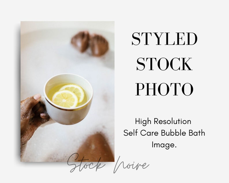May include: A person relaxing in a bubble bath, holding a white mug with lemon slices in it.
