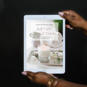 May include: A digital tablet displaying a self-care tips and tricks guide with the text "YOUR BUSINESS NAME Self Care Tips & Tricks A LIST OF OUR BEST TIPS TO IMPLEMENT TODAY" on a white background. The image shows a lit candle on a silver tray with white flowers and a white towel.