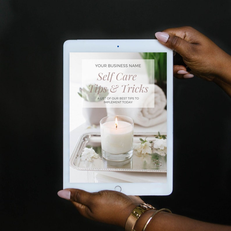 May include: A digital tablet displaying a self-care tips and tricks guide with the text "YOUR BUSINESS NAME Self Care Tips & Tricks A LIST OF OUR BEST TIPS TO IMPLEMENT TODAY" on a white background. The image shows a lit candle on a silver tray with white flowers and a white towel.