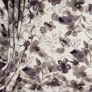 May include: A white fabric with a floral pattern in shades of brown and purple. The fabric is folded and shows the pattern repeating.