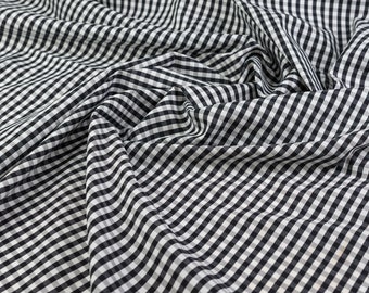 May include: Black and white gingham fabric with a checkered pattern. The fabric is folded and wrinkled, showing the texture of the material.