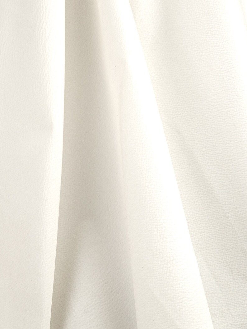 May include: White fabric with a textured surface. The fabric is folded and draped, creating soft folds and shadows.