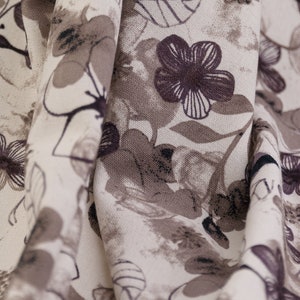 May include: A close-up of a white fabric with a brown floral pattern. The fabric is folded and the pattern is visible on both sides of the fold.