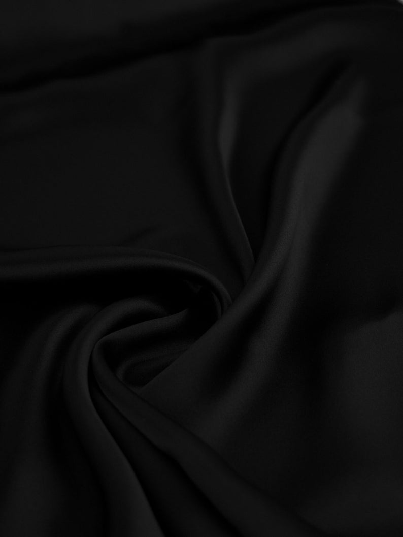 May include: Close-up of a smooth, black fabric with soft folds and wrinkles. The fabric has a luxurious, silky texture.