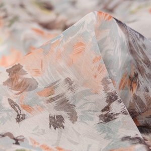 Puede incluir: Primer plano de una tela transparente con estampado floral en tonos melocotón, marrón y azul. La tela es suave y fluida, con una textura delicada.