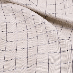 May include: A close-up of a beige fabric with a fine, dark blue checkered pattern. The fabric is woven with a herringbone texture.