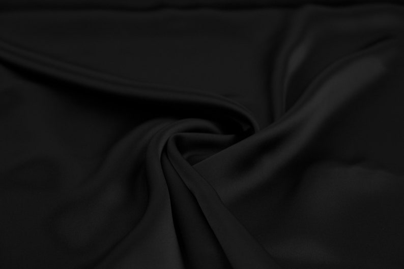 May include: Black fabric with smooth, silky texture, draped and folded to create soft curves and folds.