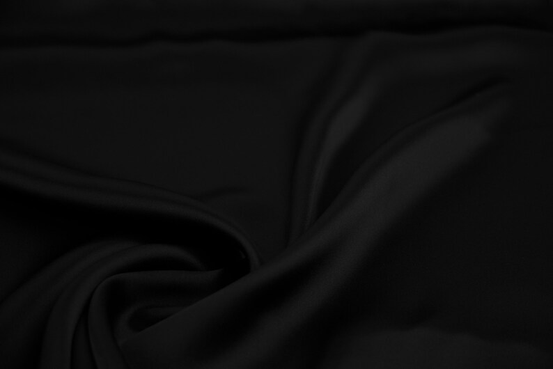 May include: A smooth, black fabric with soft folds and wrinkles. The fabric has a luxurious, silky texture.