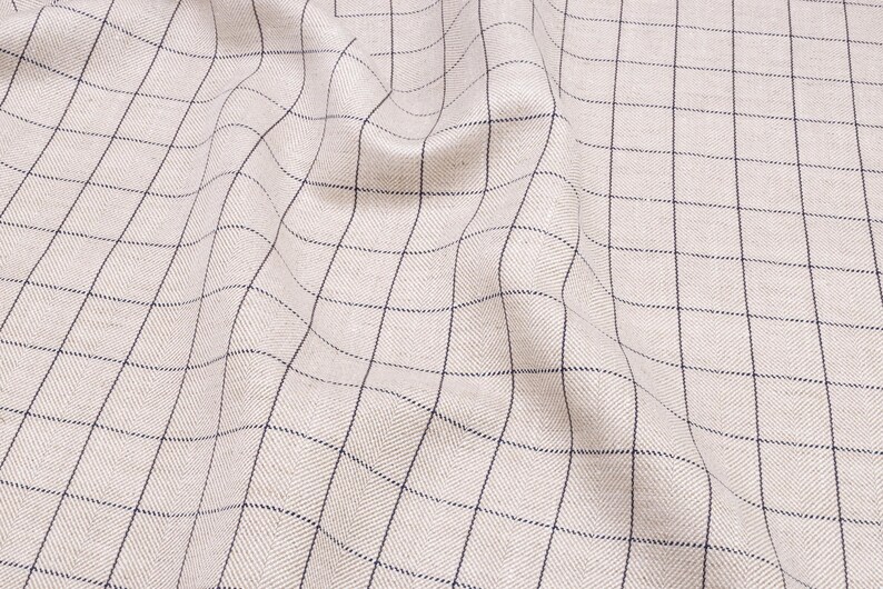 May include: A close-up of a beige fabric with a black and white checkered pattern. The fabric is wrinkled and has a soft, textured appearance.