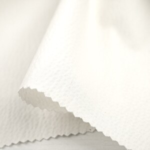 May include: White fabric with a textured surface. The fabric is folded over itself, creating a wave-like shape.