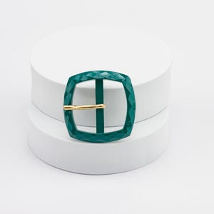 May include: A green metal buckle with a diamond pattern and a gold metal bar.