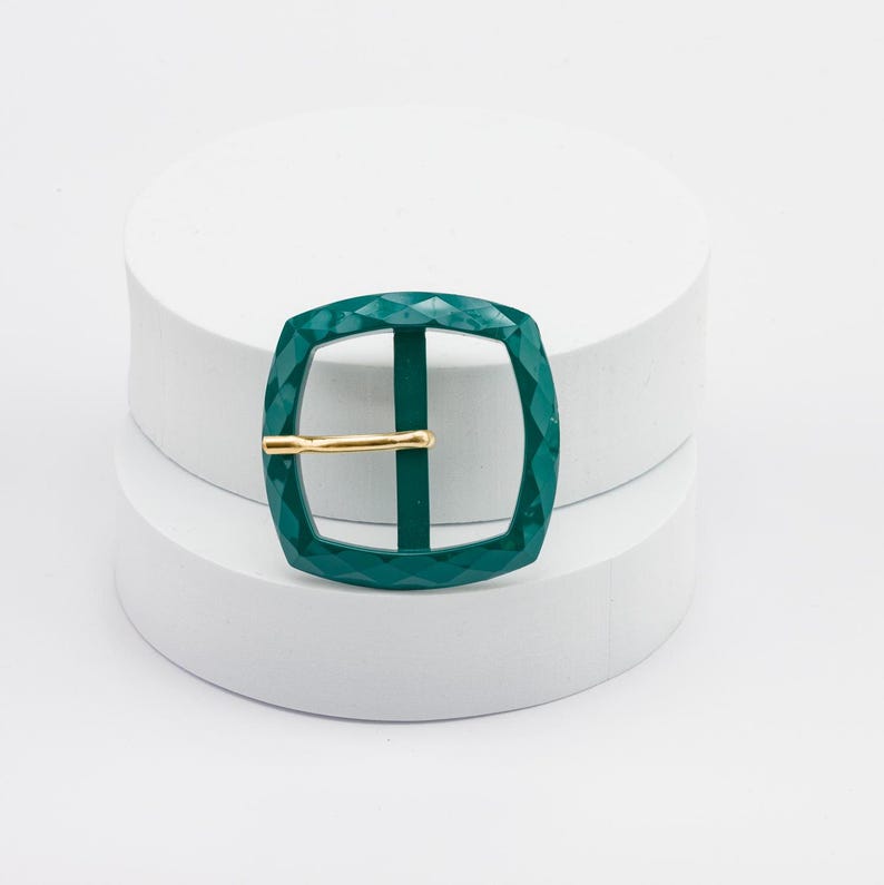 May include: A green metal buckle with a diamond pattern and a gold metal bar.