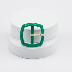 May include: A green metal buckle with a textured surface and a gold metal bar.