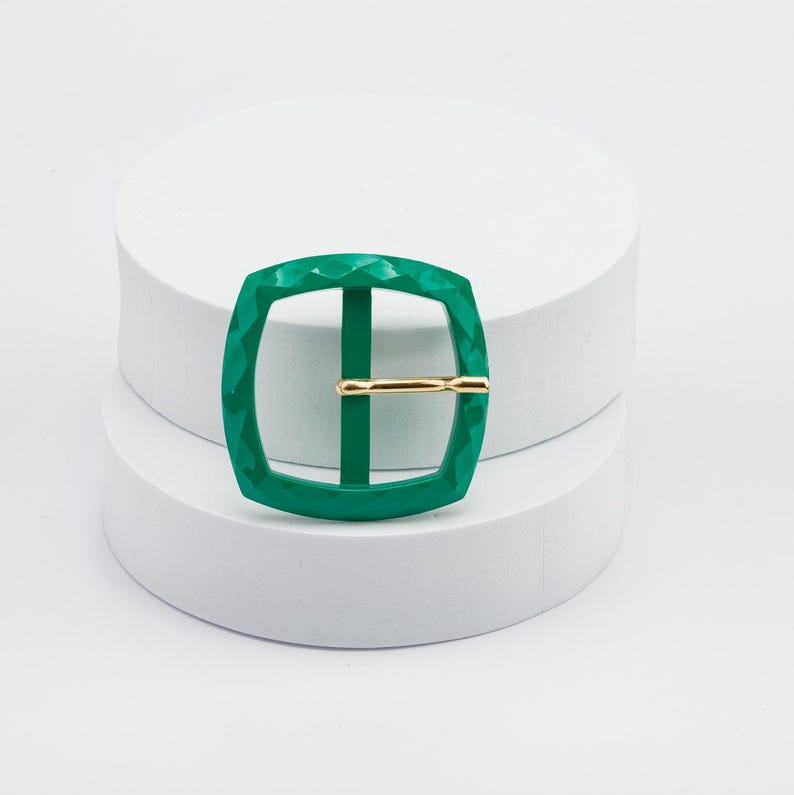 May include: A green metal buckle with a textured surface and a gold metal bar.