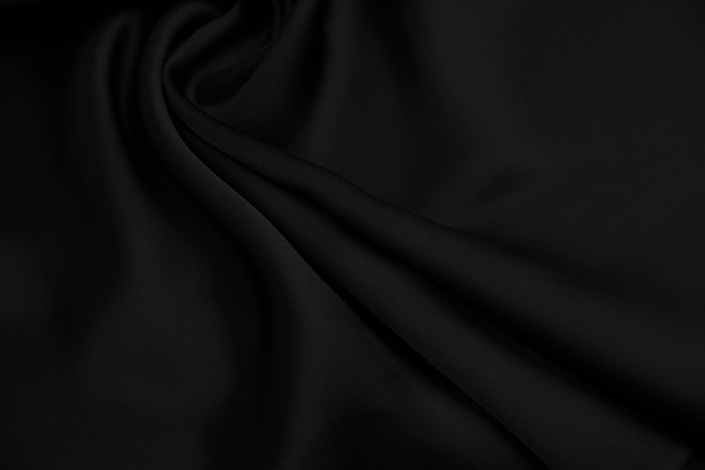 May include: Black fabric with a smooth, silky texture. The fabric is draped and folded, creating soft curves and folds.