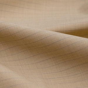 May include: Close-up of a tan fabric with fine, blue pinstripes. The material is folded, revealing its texture and weave. The image suggests a high-quality textile, potentially for tailoring or clothing.