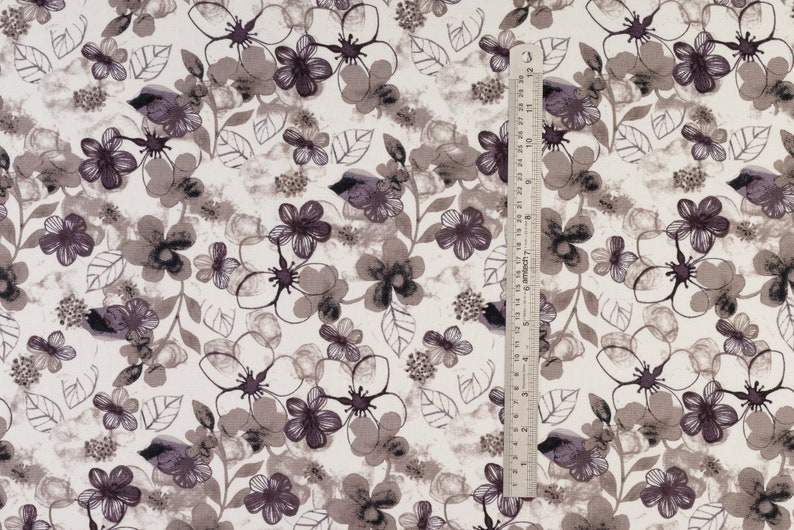 May include: White fabric with a repeating pattern of brown and purple flowers and leaves. A ruler is visible on the right side of the image.