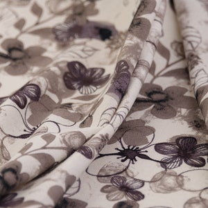 May include: Close-up of a beige fabric with a brown floral pattern. The fabric is folded and has a soft, textured surface.