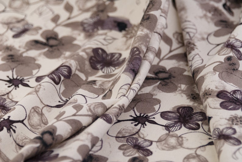 May include: Close-up of a beige fabric with a brown floral pattern. The fabric is folded and has a soft, textured surface.