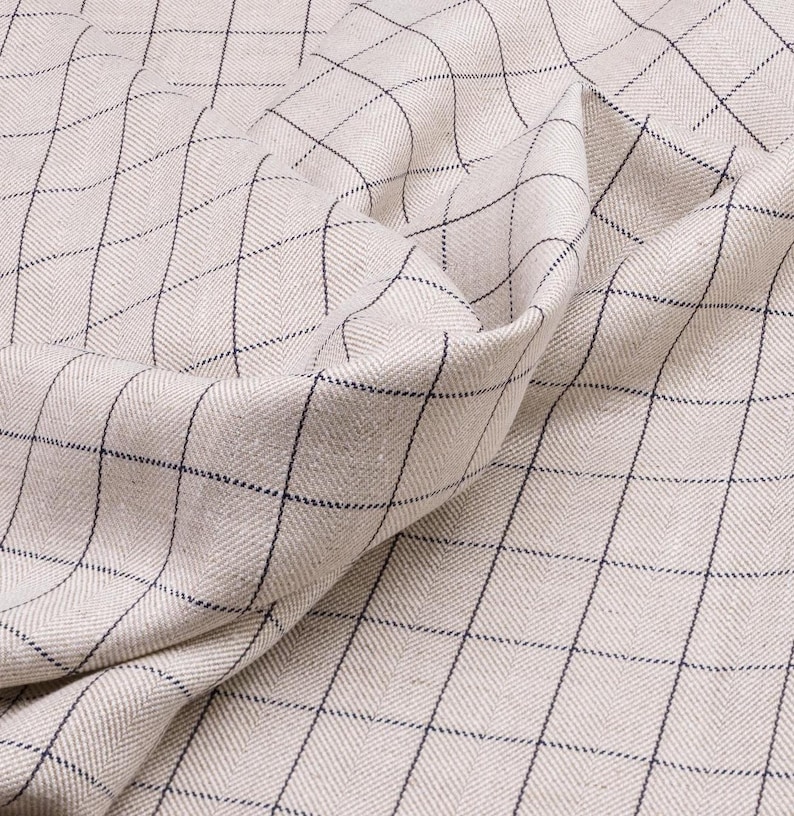May include: A close-up of a beige fabric with a black and white checkered pattern. The fabric is woven with a herringbone texture.