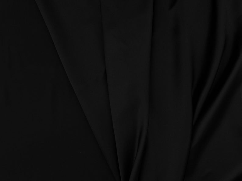 May include: Black fabric with a smooth, silky texture. The fabric is folded and draped, creating soft folds and curves.